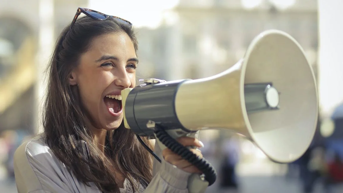 cheerful young woman screaming into megaphone